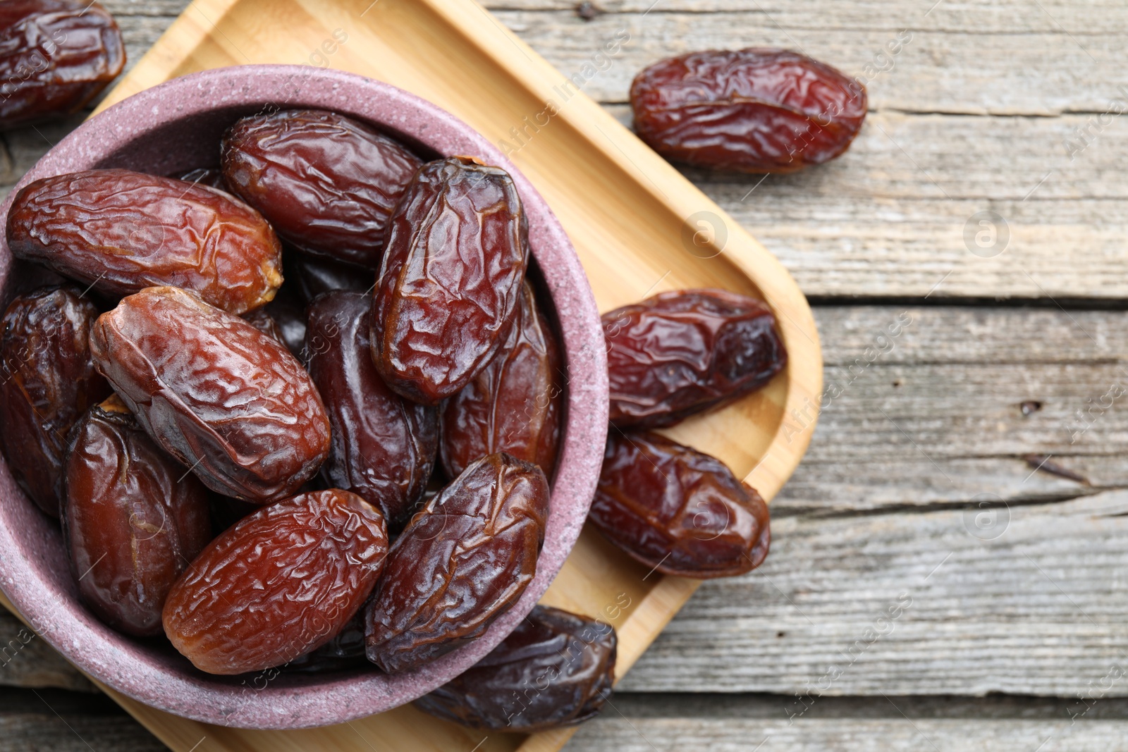 Photo of Many tasty dried dates in bowl on wooden table, top view