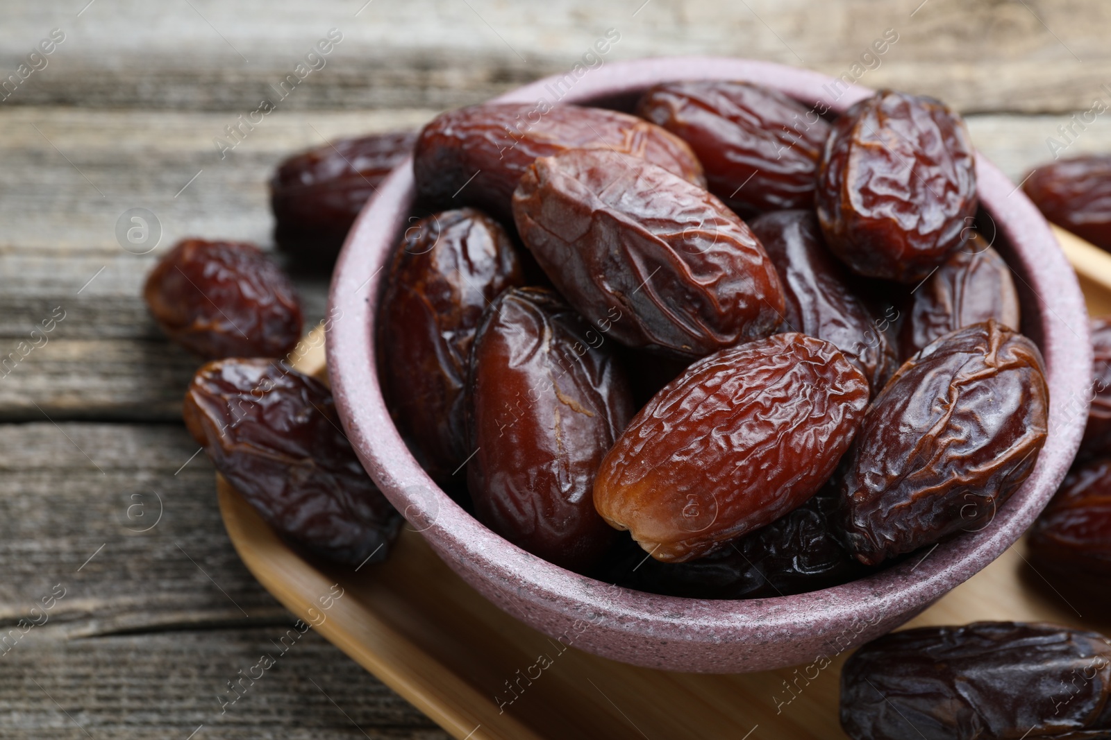 Photo of Many tasty dried dates in bowl on wooden table, closeup