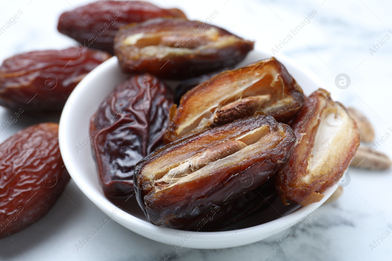 Photo of Many tasty dried dates in bowl on light table, closeup