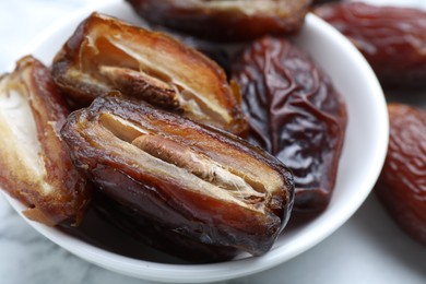 Photo of Many tasty dried dates in bowl on light table, closeup