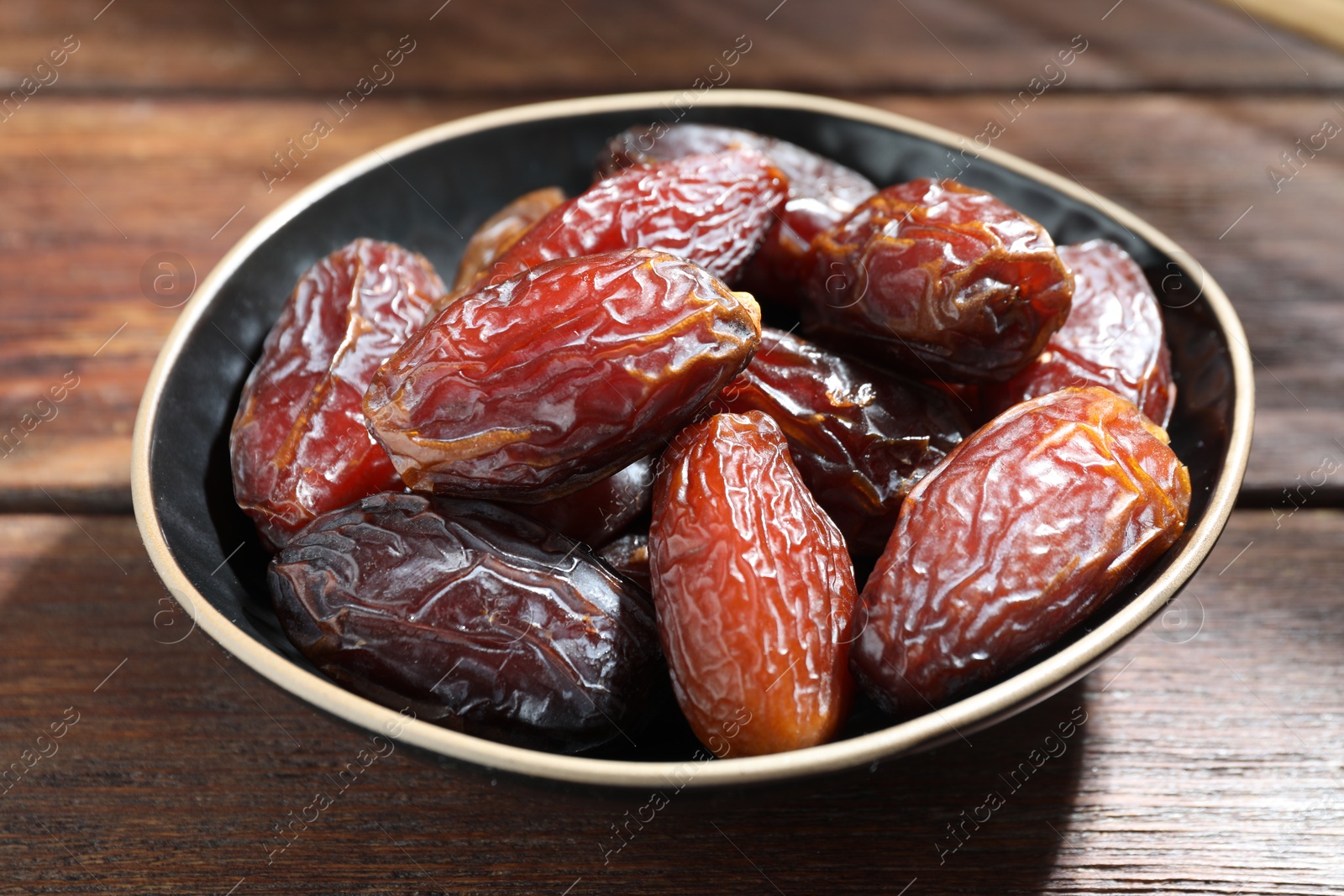 Photo of Many tasty dried dates in bowl on wooden table, closeup