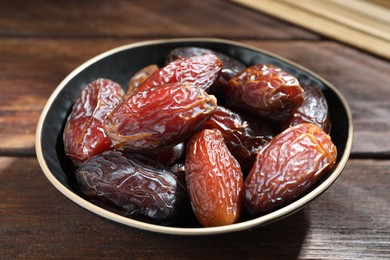 Photo of Many tasty dried dates in bowl on wooden table, closeup