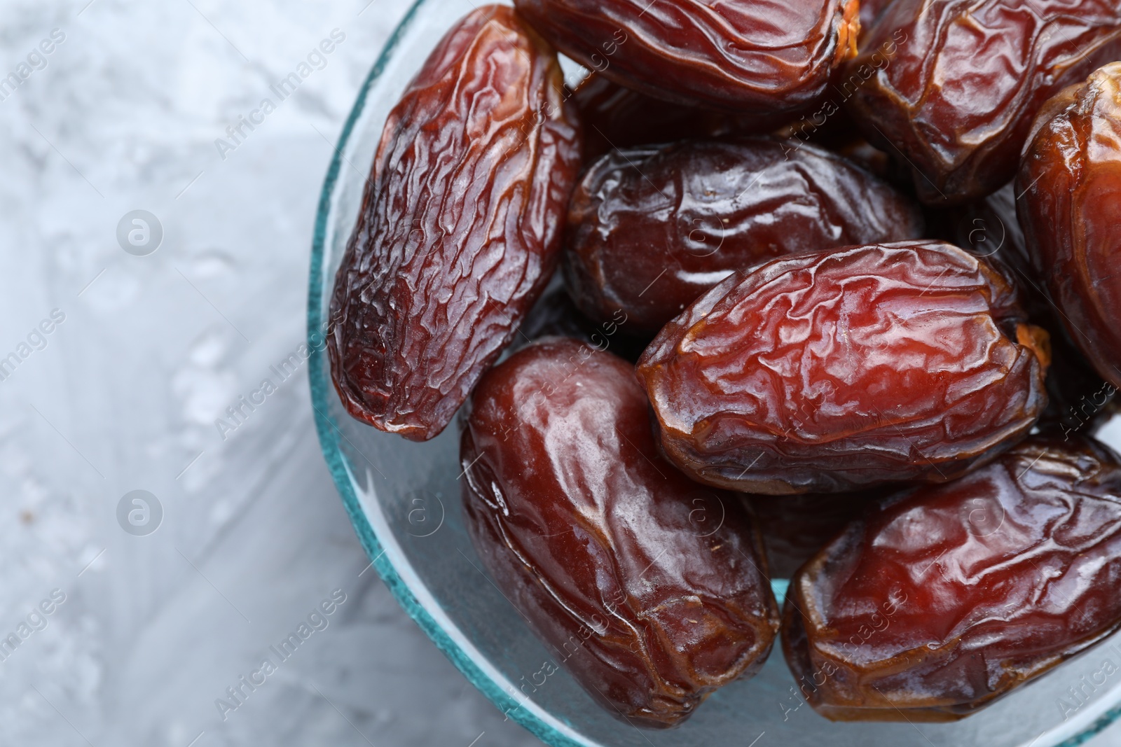 Photo of Many tasty dried dates in bowl on gray textured table, top view