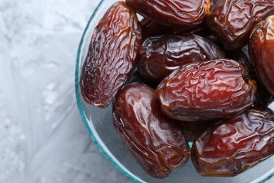 Photo of Many tasty dried dates in bowl on gray textured table, top view