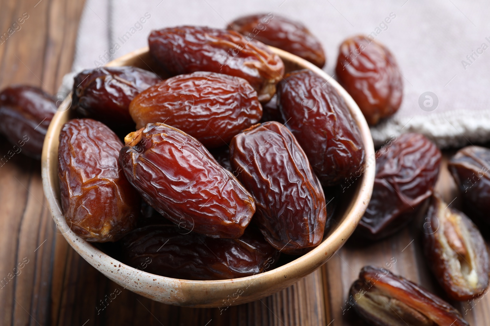 Photo of Many tasty dried dates in bowl on wooden table, closeup