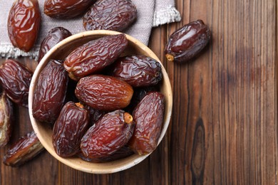 Photo of Many tasty dried dates in bowl on wooden table, top view. Space for text