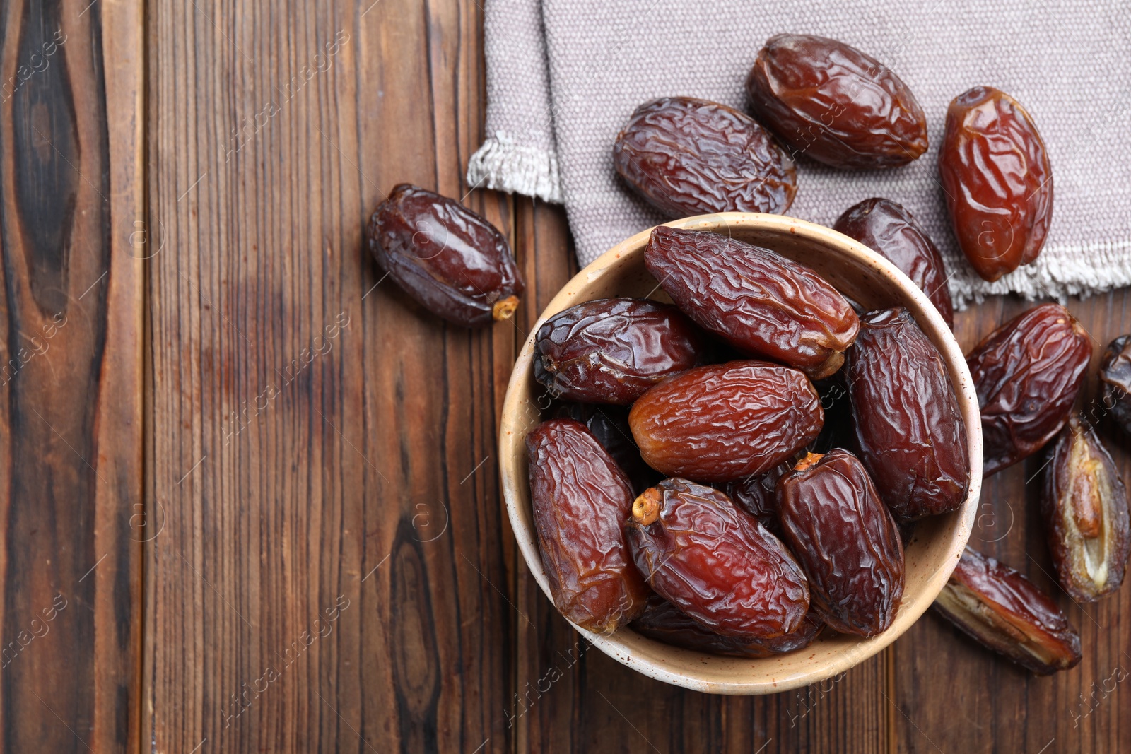 Photo of Many tasty dried dates in bowl on wooden table, top view. Space for text