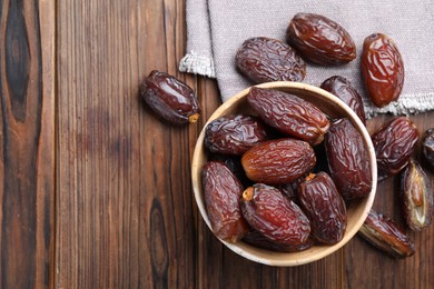 Photo of Many tasty dried dates in bowl on wooden table, top view. Space for text