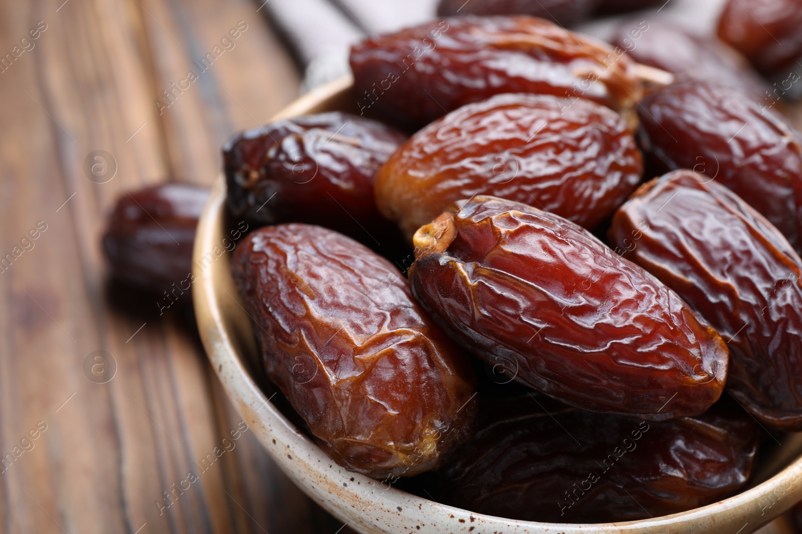 Photo of Many tasty dried dates in bowl on brown table, closeup