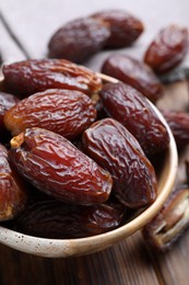 Photo of Many tasty dried dates in bowl on wooden table, closeup