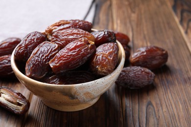 Photo of Many tasty dried dates in bowl on wooden table, closeup