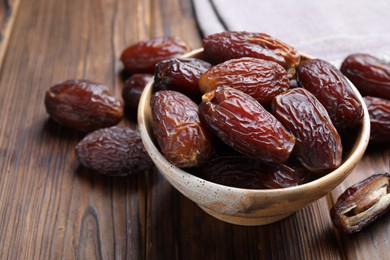 Photo of Many tasty dried dates in bowl on wooden table, closeup