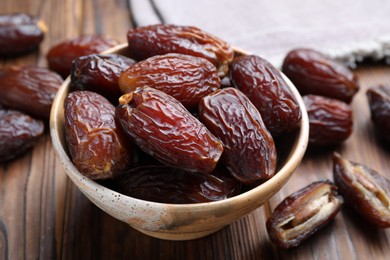 Photo of Many tasty dried dates in bowl on wooden table, closeup