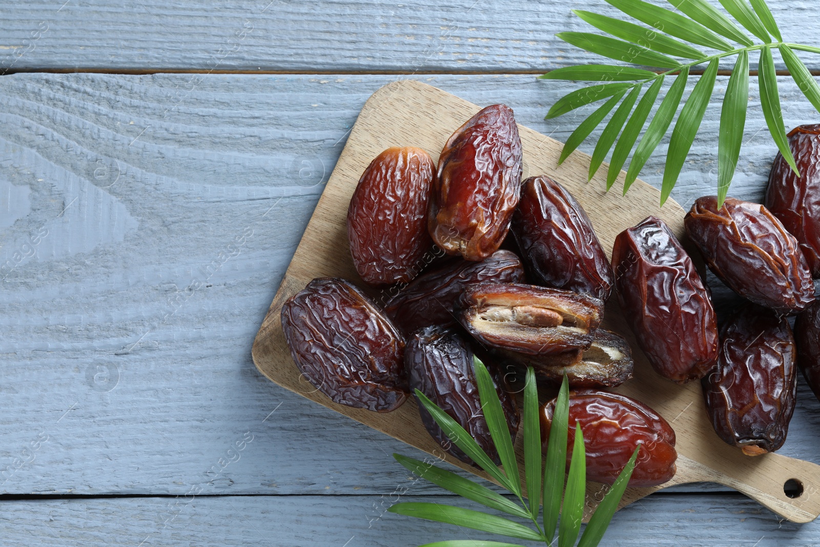 Photo of Many tasty dried dates and leaves on blue wooden table, top view. Space for text