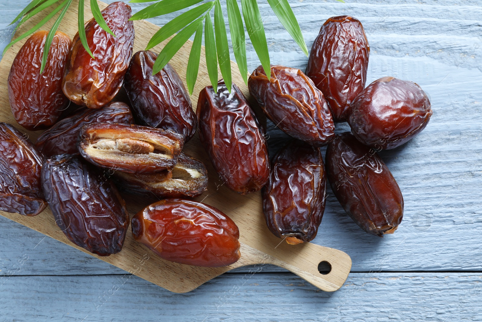 Photo of Many tasty dried dates and leaves on blue wooden table, top view