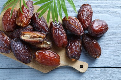 Photo of Many tasty dried dates and leaves on blue wooden table, top view