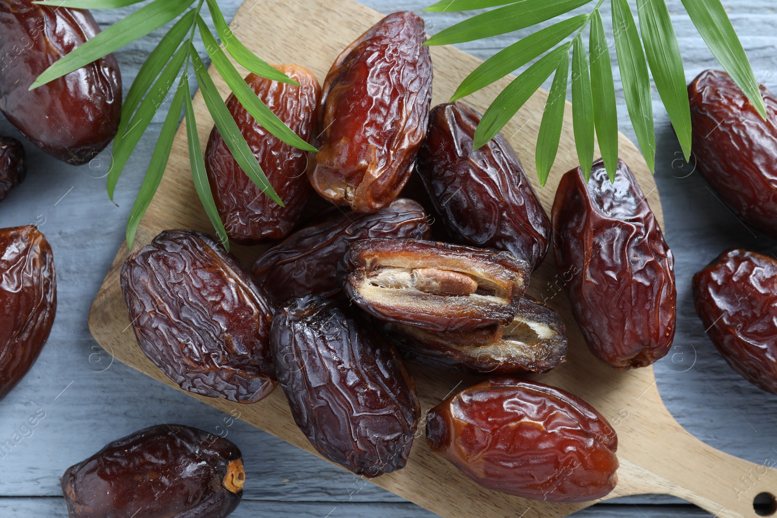 Photo of Many tasty dried dates and leaves on blue wooden table, top view