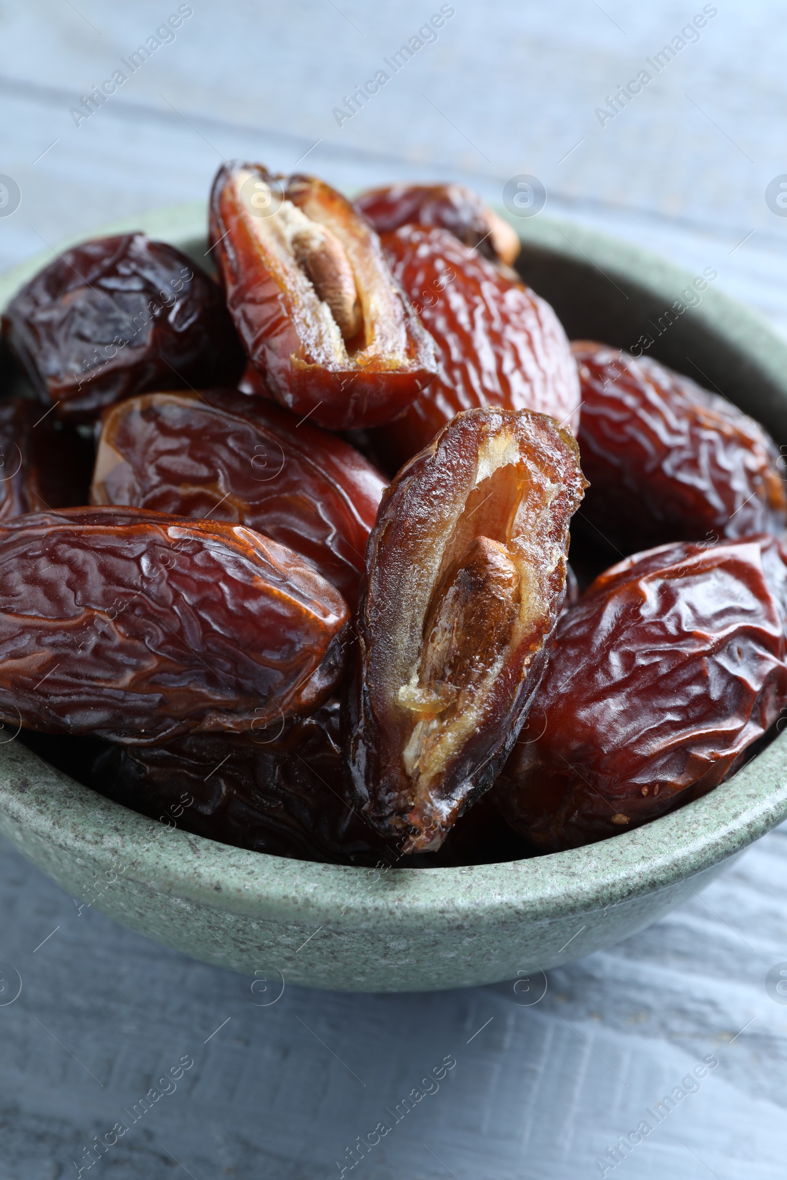 Photo of Many tasty dried dates in bowl on blue wooden table, closeup