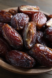 Photo of Many tasty dried dates in bowl on wooden table, closeup