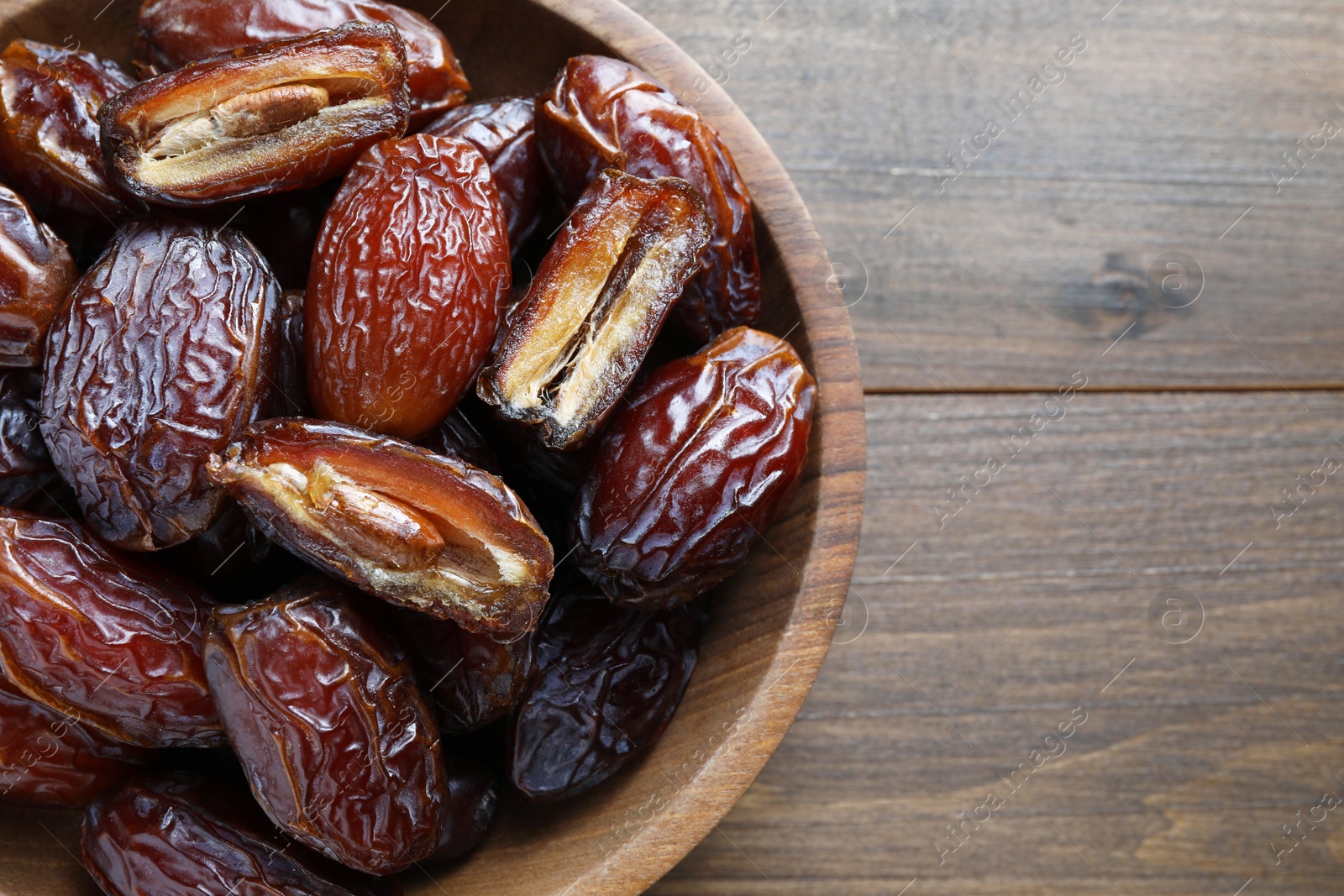 Photo of Many tasty dried dates in bowl on wooden table, top view. Space for text