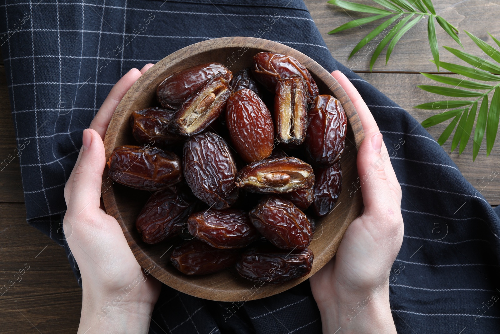 Photo of Woman with bowl of tasty dried dates at wooden table, top view