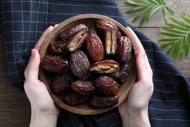 Photo of Woman with bowl of tasty dried dates at wooden table, top view