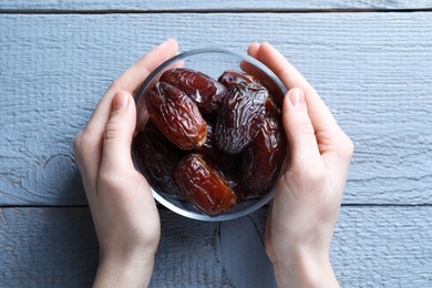 Photo of Woman with bowl of tasty dried dates at blue wooden table, top view