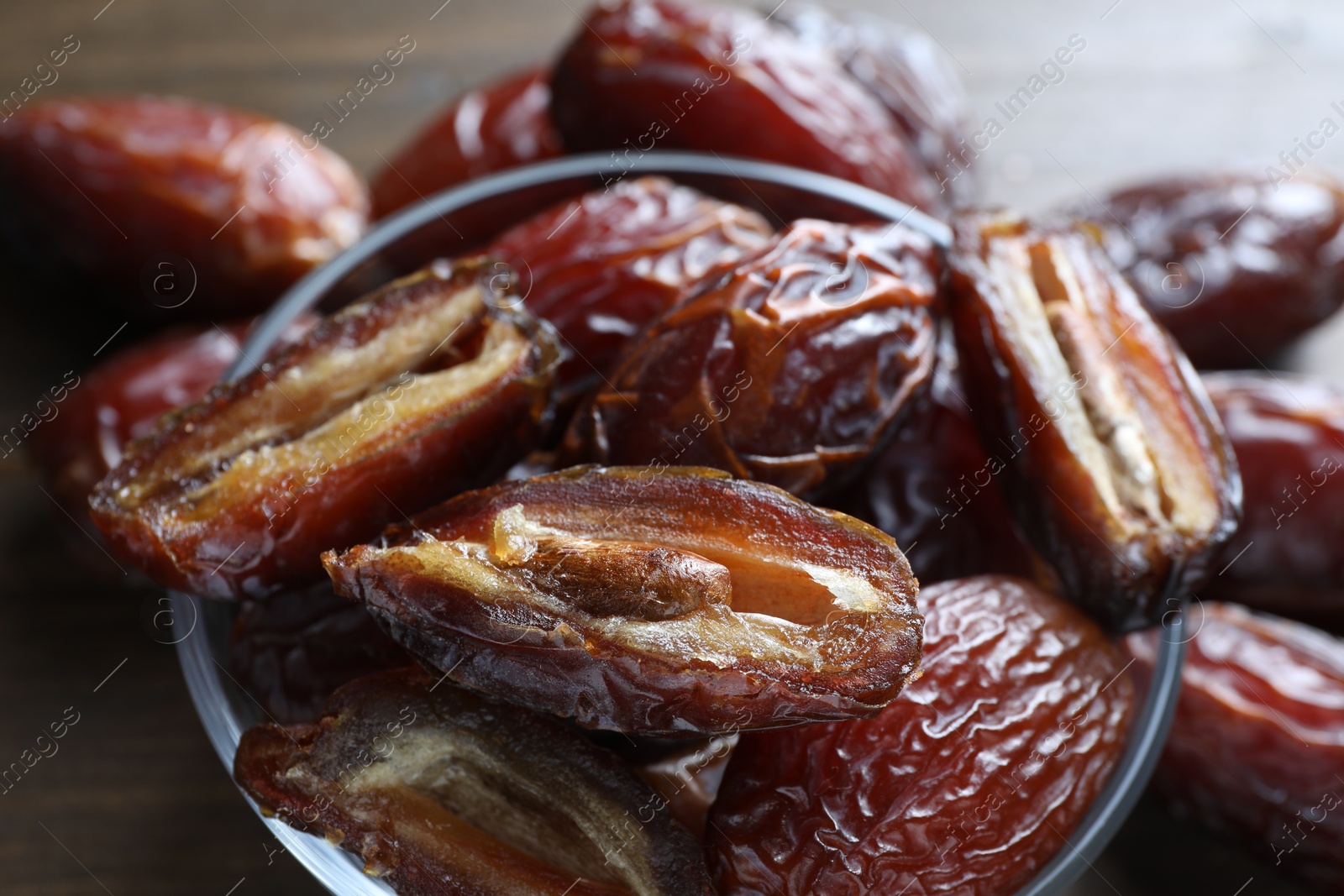 Photo of Many tasty dried dates in bowl on brown table, closeup