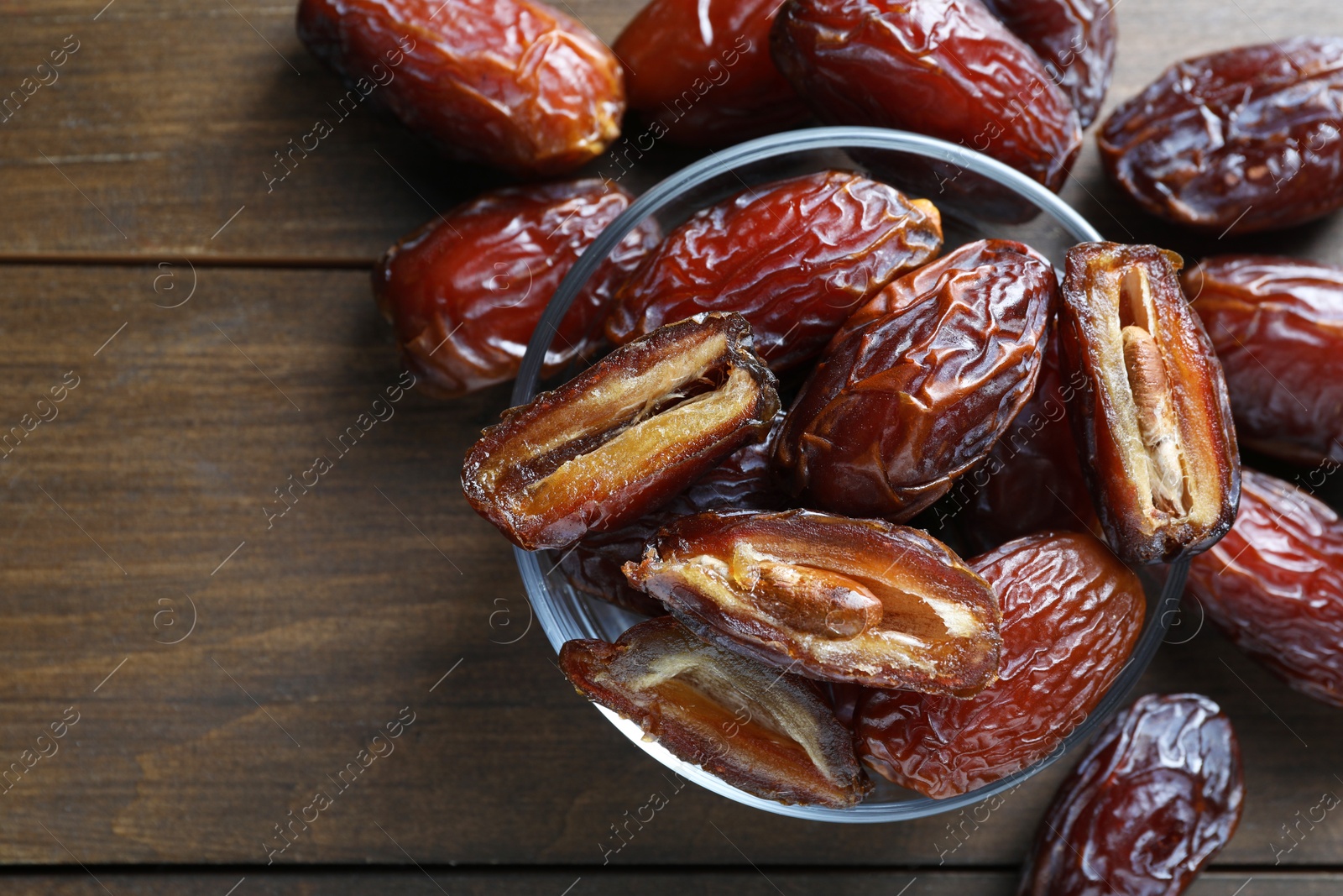 Photo of Many tasty dried dates in bowl on wooden table, top view. Space for text