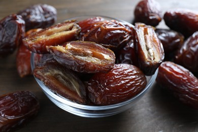 Photo of Many tasty dried dates in bowl on wooden table, closeup