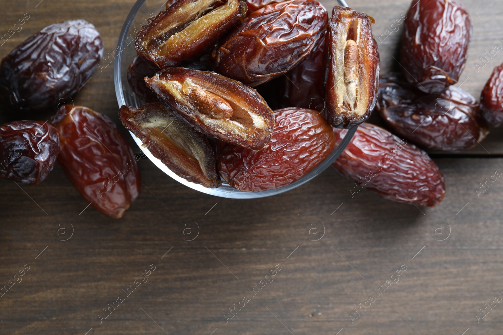 Photo of Many tasty dried dates in bowl on wooden table, top view. Space for text