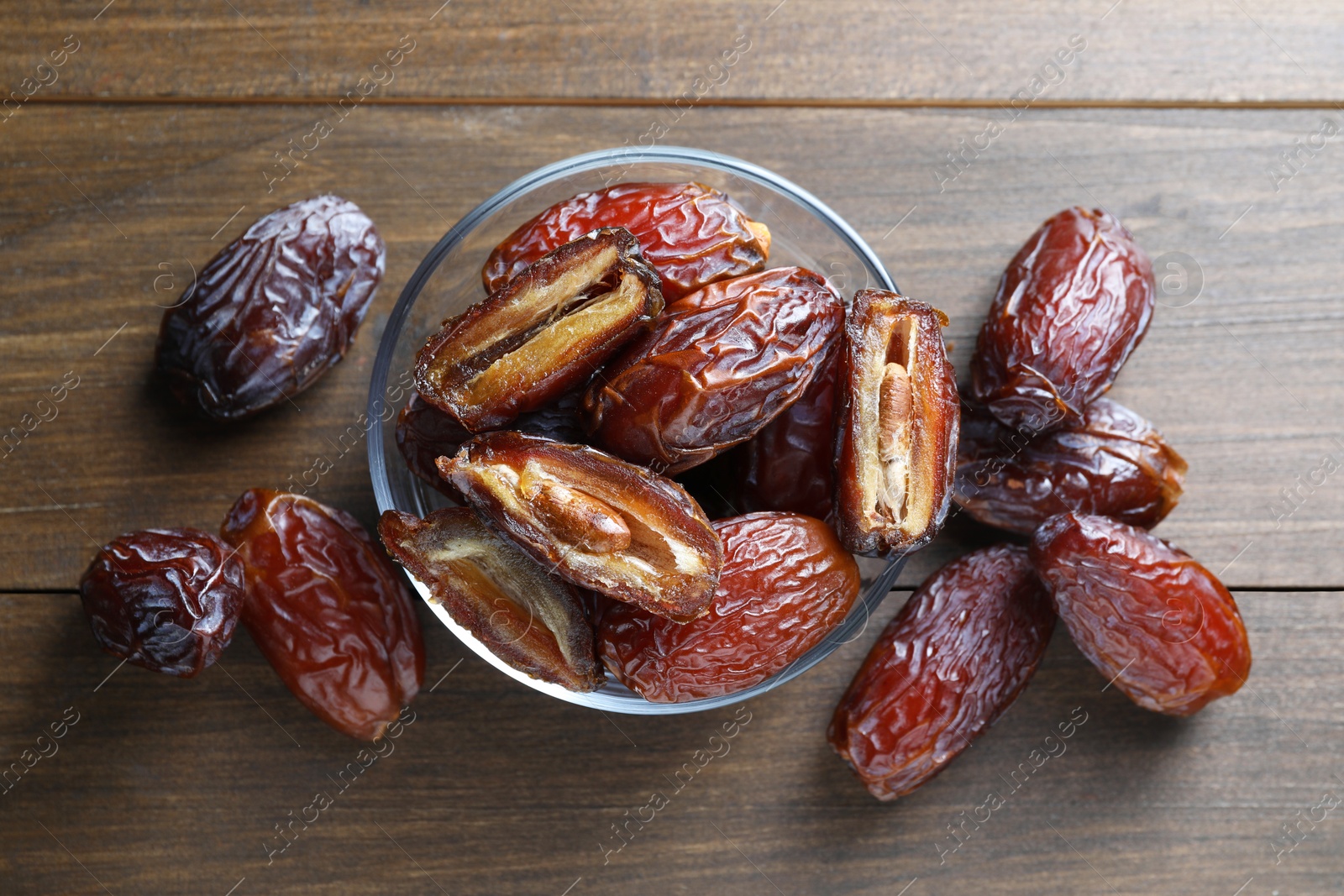 Photo of Many tasty dried dates in bowl on wooden table, top view