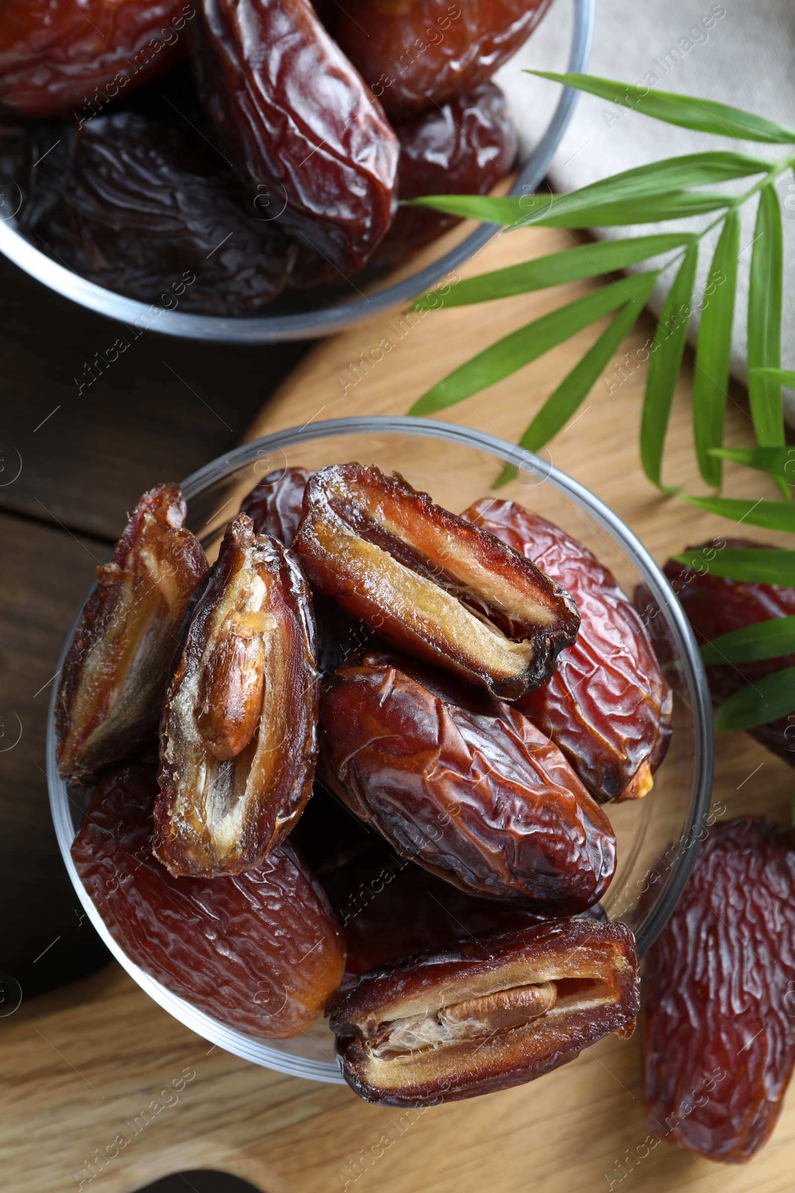 Photo of Many tasty dried dates in bowls and leaves on table, top view