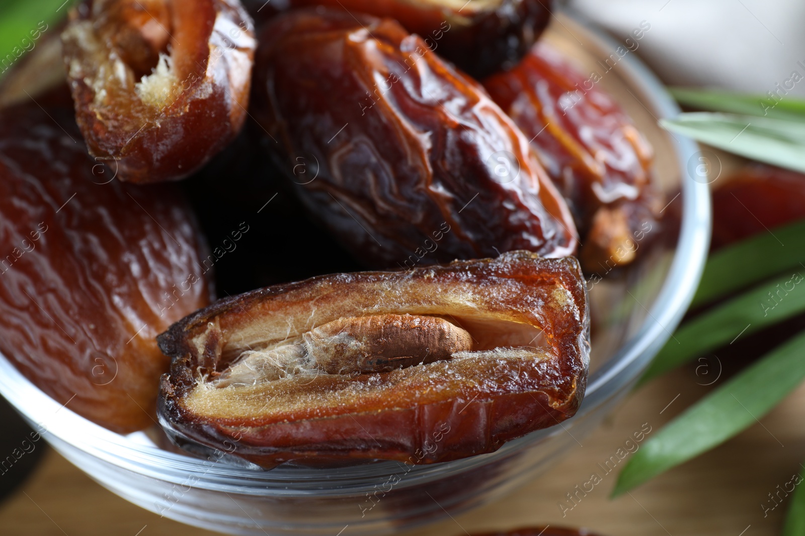 Photo of Many tasty dried dates in bowl and leaf on table, closeup