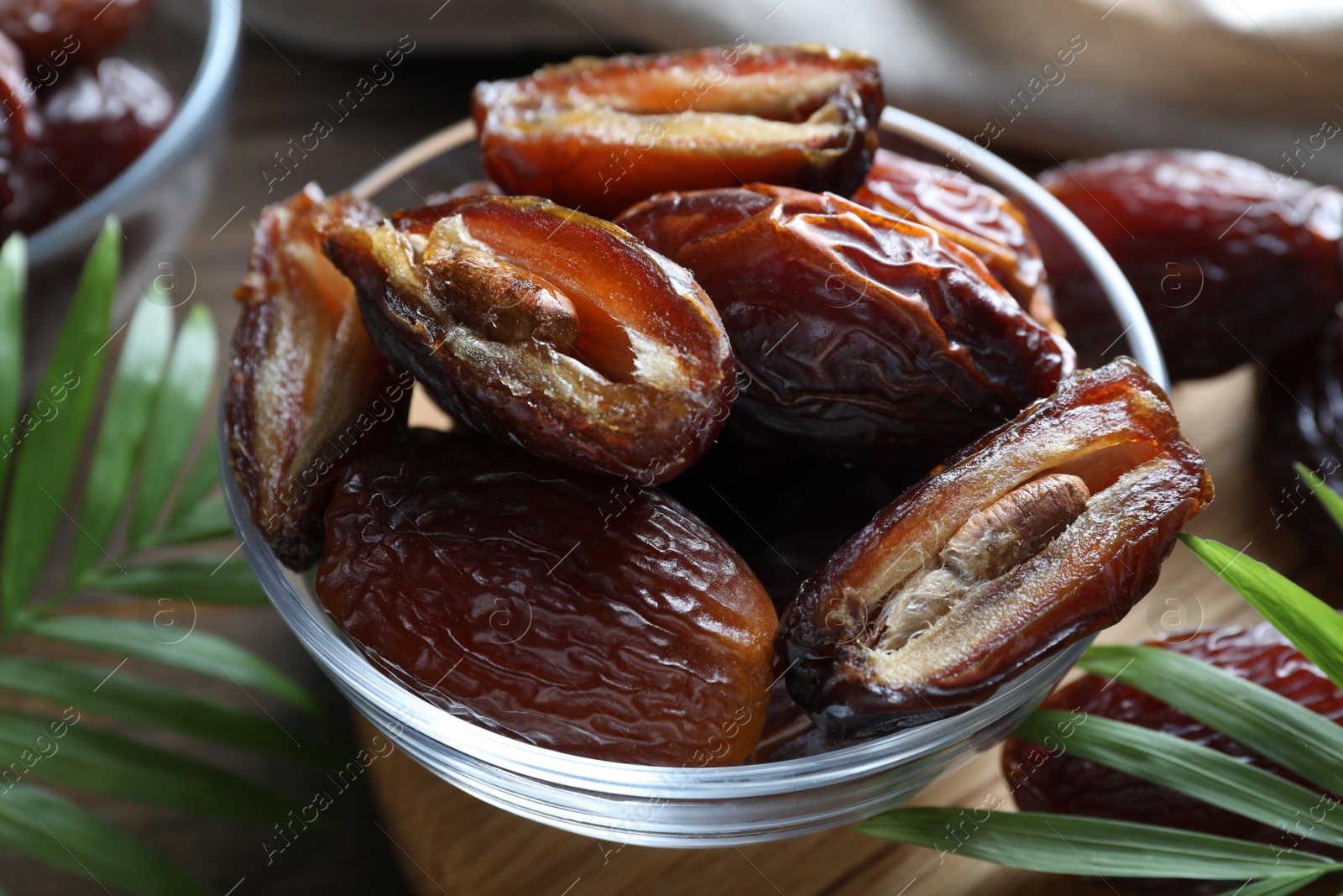 Photo of Many tasty dried dates in bowl and leaves on table, closeup