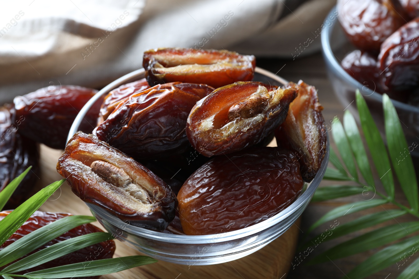 Photo of Many tasty dried dates in bowl and leaves on table, closeup