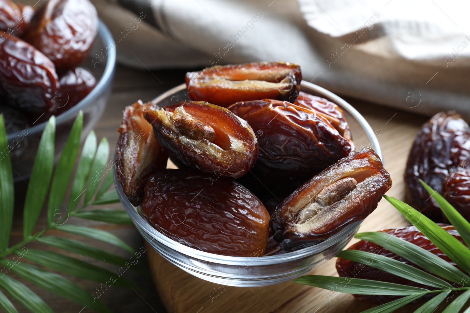 Photo of Many tasty dried dates in bowls and leaves on table, closeup