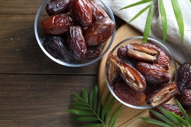 Photo of Many tasty dried dates in bowls and leaves on wooden table, flat lay