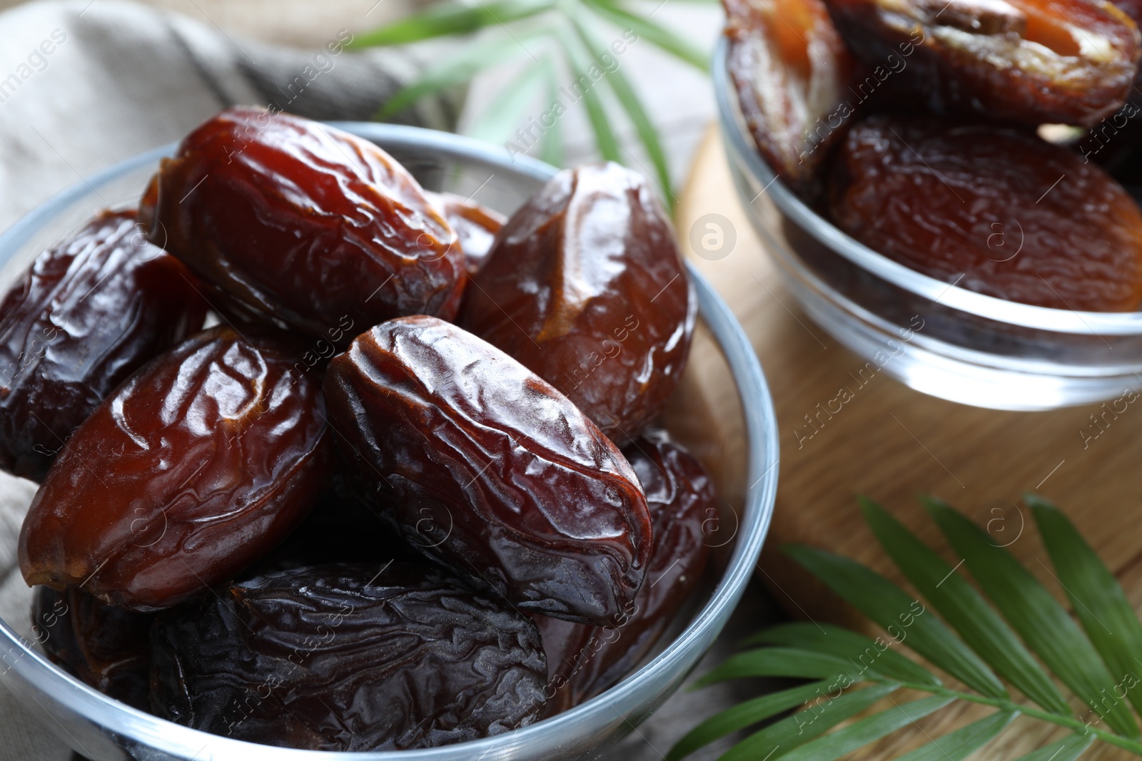 Photo of Many tasty dried dates in bowls and leaves on table, closeup