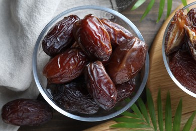 Photo of Many tasty dried dates in bowls and leaves on table, flat lay