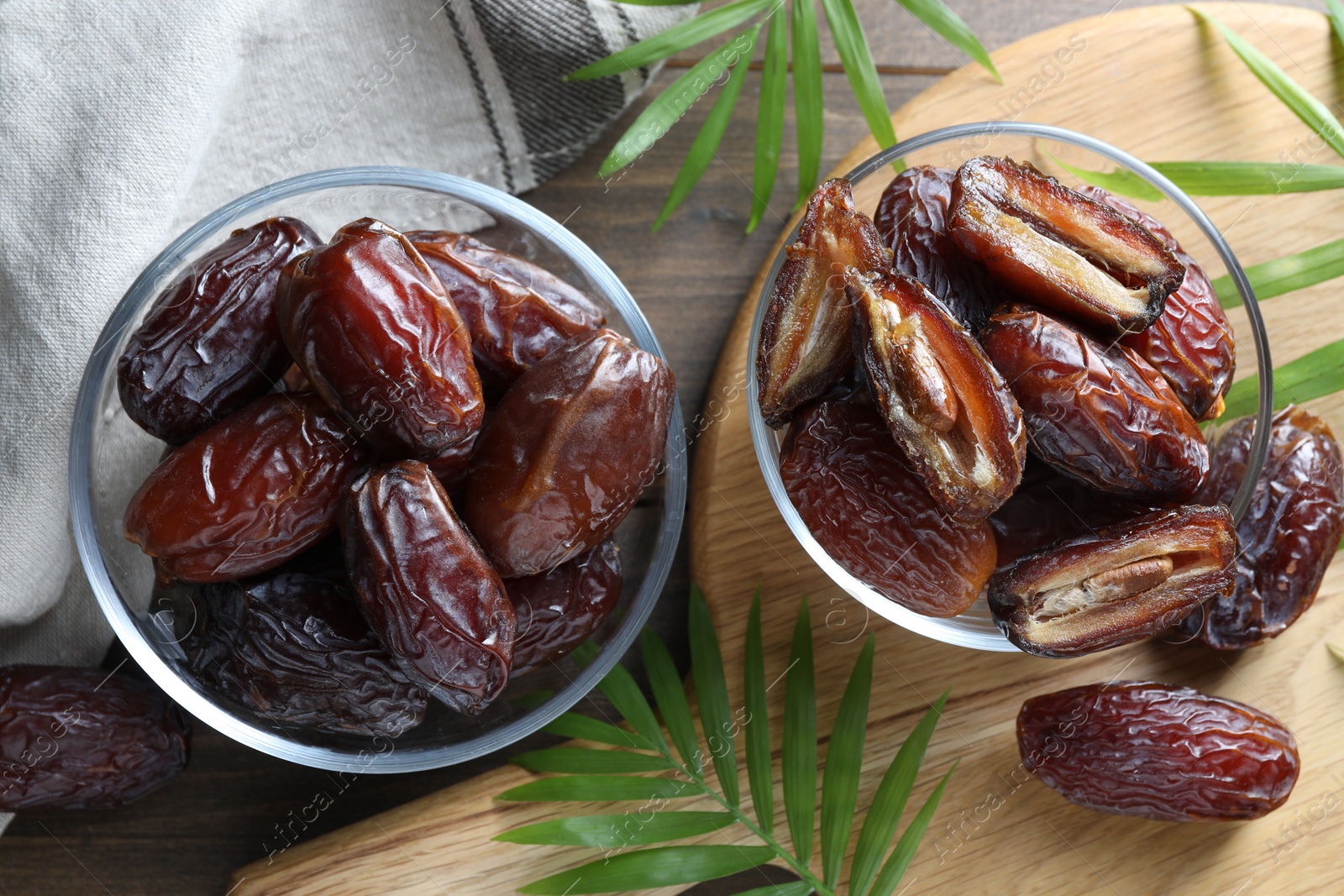 Photo of Many tasty dried dates in bowls and leaves on wooden table, flat lay