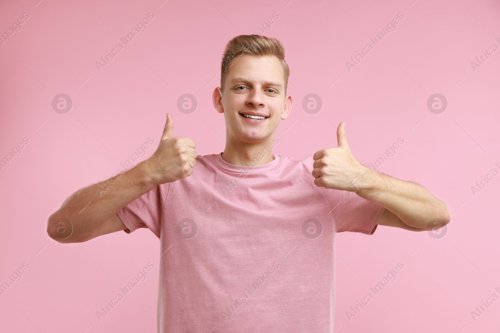 Photo of Happy man showing thumbs up on pink background. Like gesture