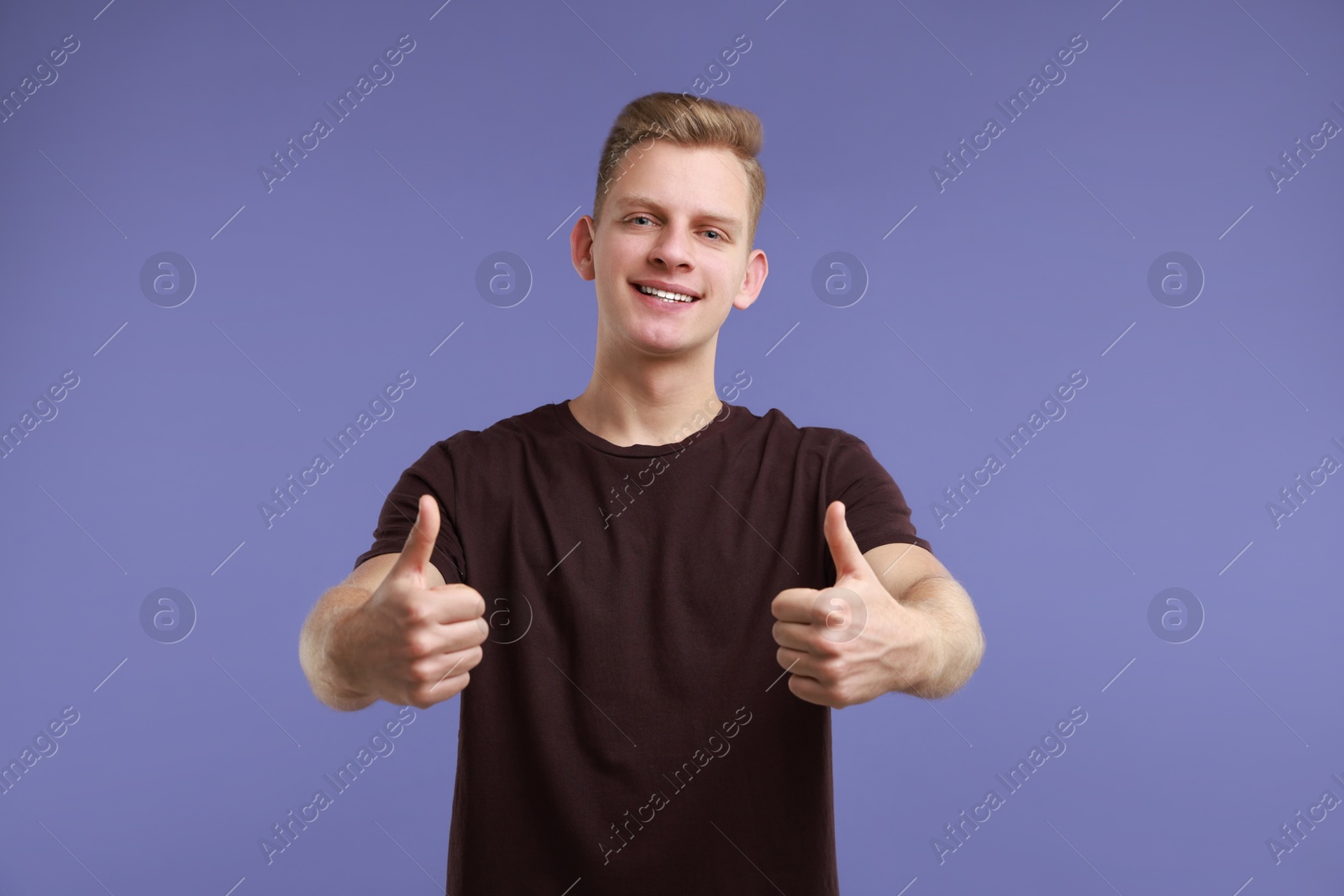 Photo of Happy man showing thumbs up on purple background. Like gesture