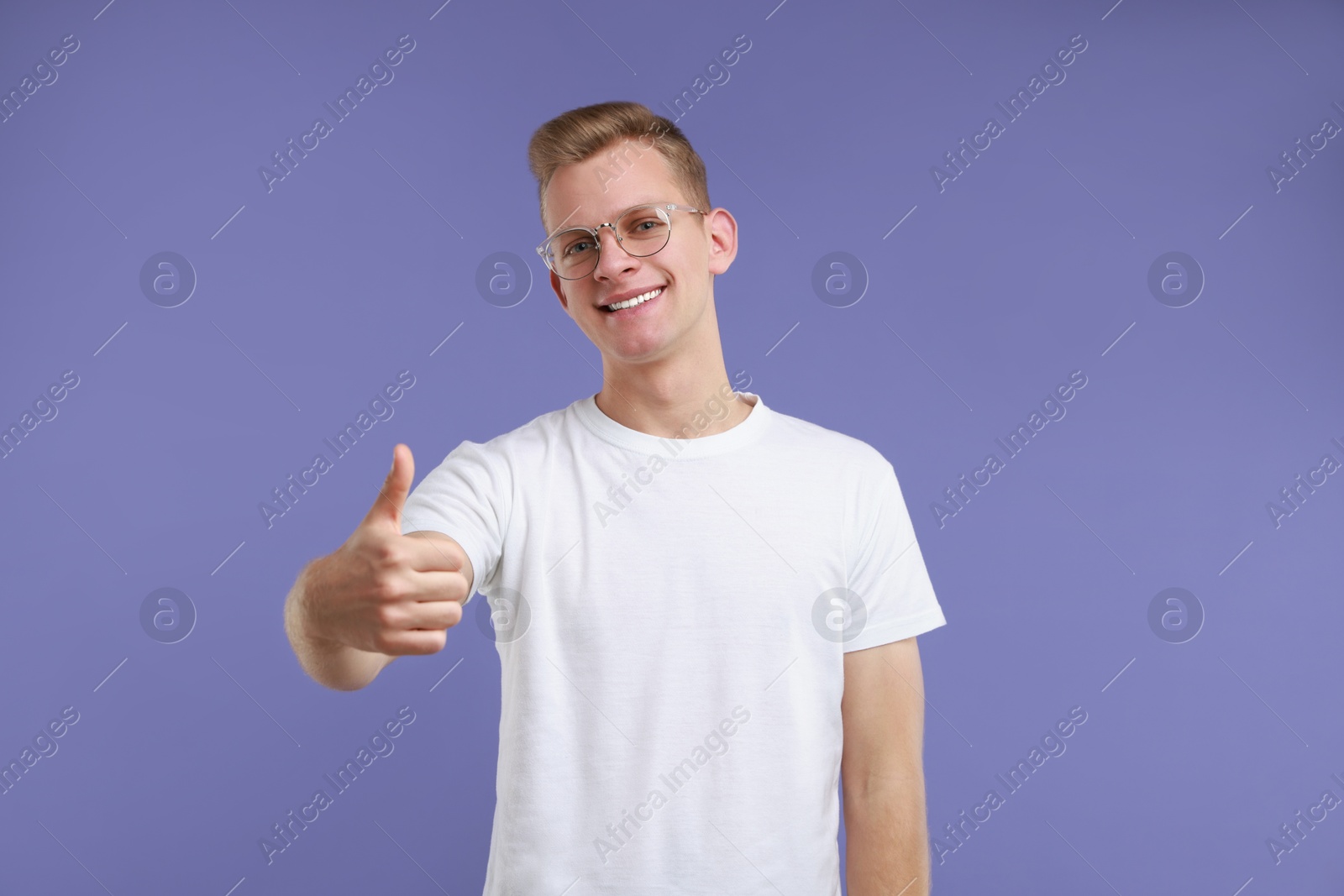 Photo of Happy man showing thumbs up on purple background. Like gesture