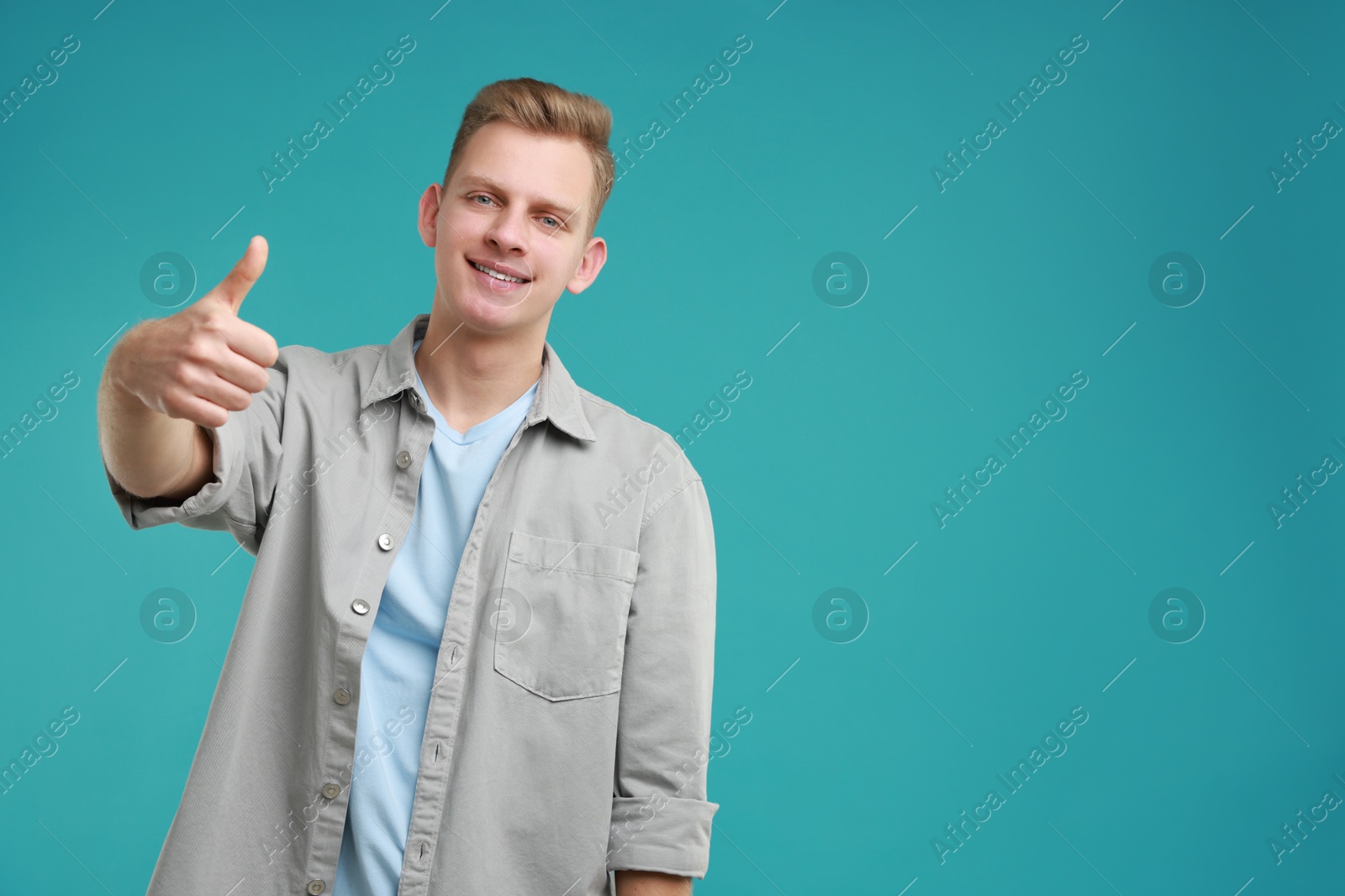 Photo of Happy man showing thumbs up on light blue background, space for text. Like gesture