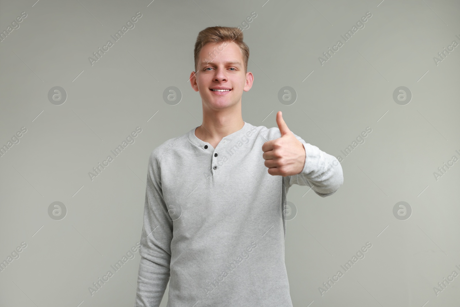 Photo of Happy man showing thumbs up on grey background. Like gesture