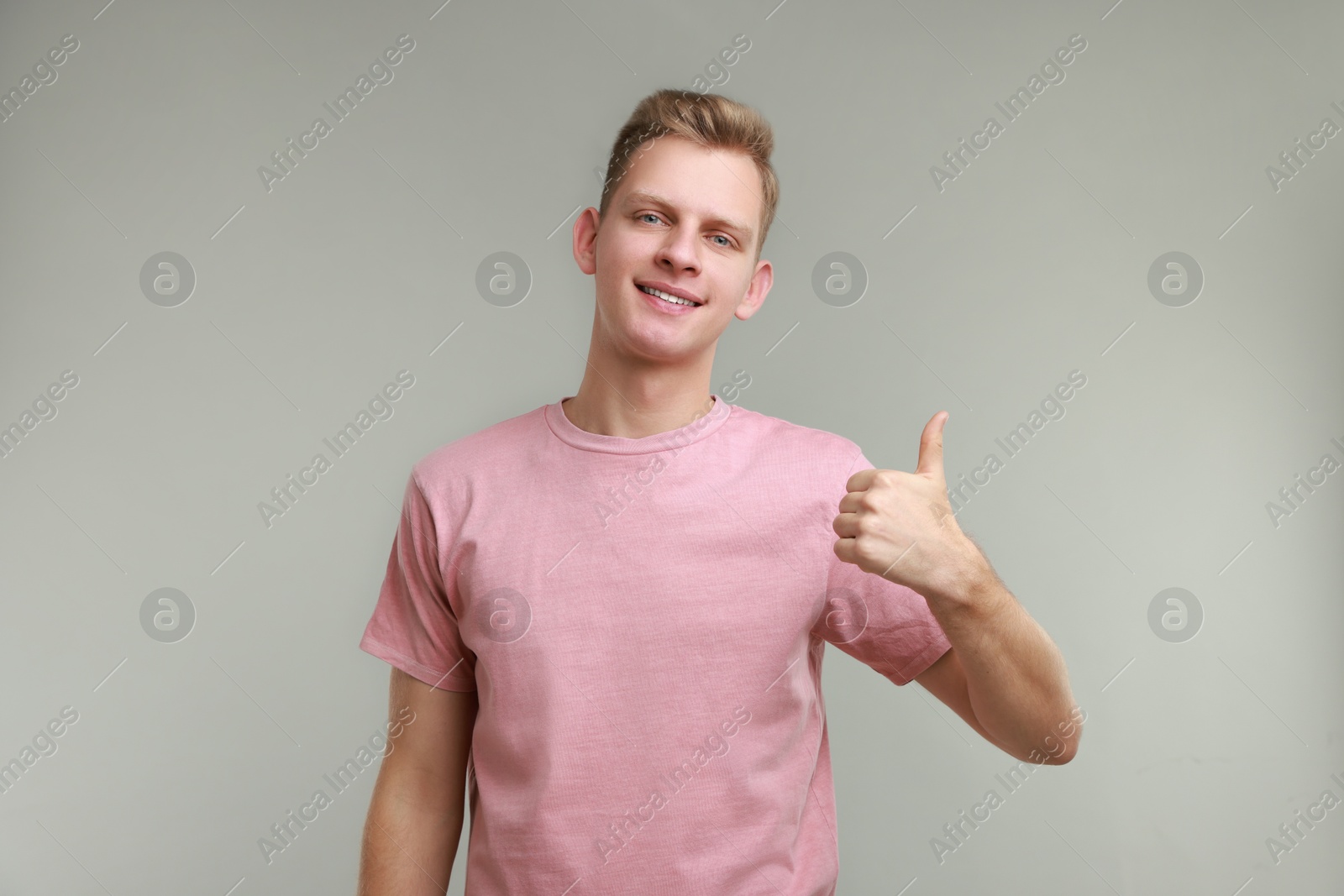 Photo of Happy man showing thumbs up on grey background. Like gesture