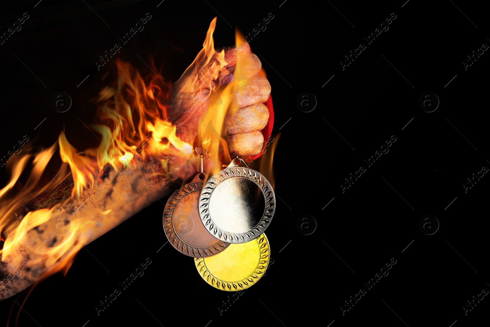 Image of Man holding gold, silver and bronze medals in his flaming hand on black background, closeup