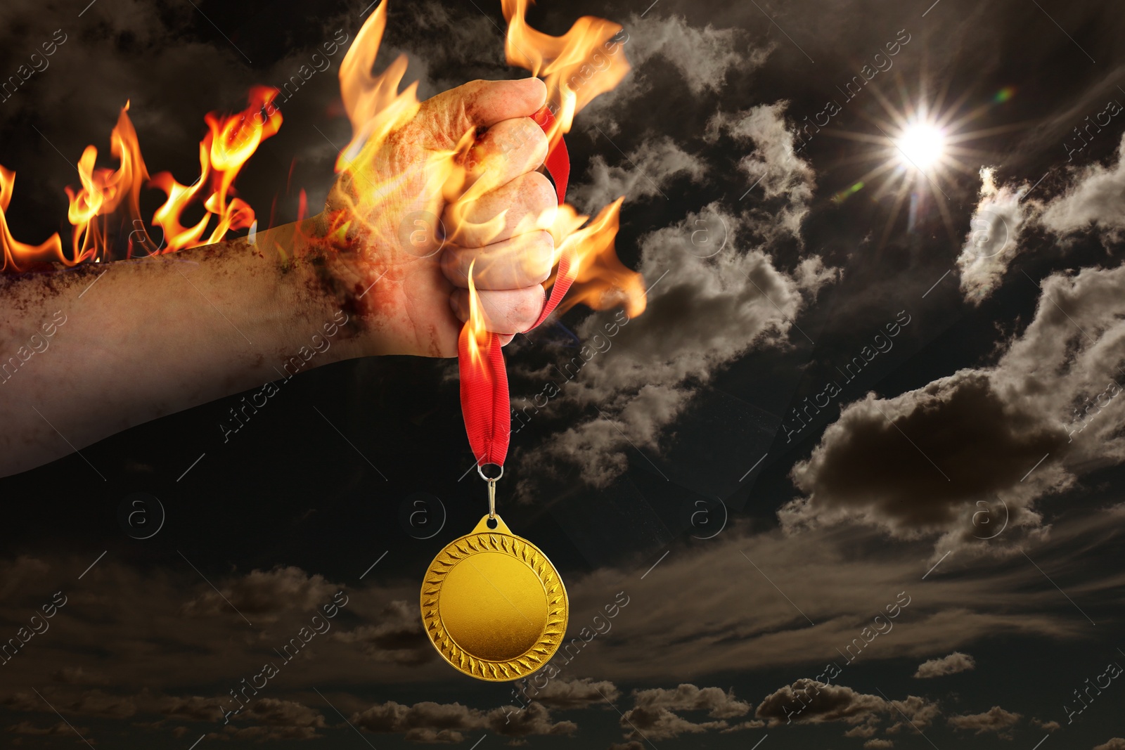 Image of Man holding gold medal in his flaming hand against darkened sky, closeup