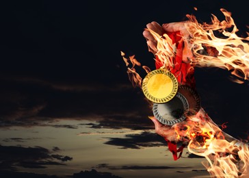 Image of Woman holding gold, silver and bronze medals in her flaming hands against darkened sky, closeup